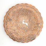 An early 20thC copper dish with a scalloped rim, punch detail and white metal inlay depicting