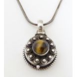 A silver pendant necklace, the pendant formed as a pill box set with tigers eye cabochon. The