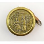 A Continental 19thC brass cased sewing tape measure, decorated with two figures in a landscape