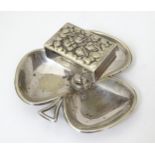A silver plate ashtray of shamrock form with raised central matchbox holder with cherub