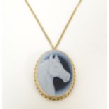 An oval pendant / brooch set with horse head decoration in a yellow metal mount with chain.