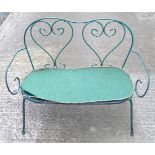 A two-seater garden bench, of wrought metal construction with two hearts forming the splat, green