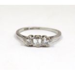 A platinum ring set with a central square cut diamond flanked by two round diamonds. Ring size