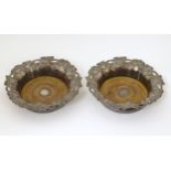 A pair of silver plate bottle coasters with fruiting vine decoration and turned wooden bases. 7 1/2"