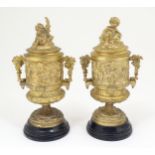 A pair of late 19thC Continental gilt lidded pedestal urns with twin handles, decorated with