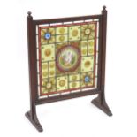 An Arts & Crafts fire screen with leaded stained glass panels to the centre and standing on shaped