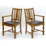 A pair of mid 20thC oak open armchairs with slatted backrests above leather upholstered seats and