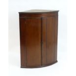 A Georgian mahogany bow fronted corner cupboard with inlaid stringing, the two doors opening to show