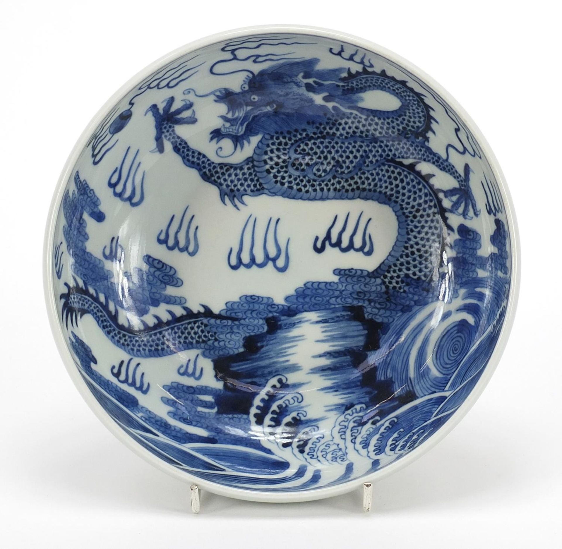 Chinese blue and white porcelain bowl hand painted with a dragon amongst clouds above waves, blue