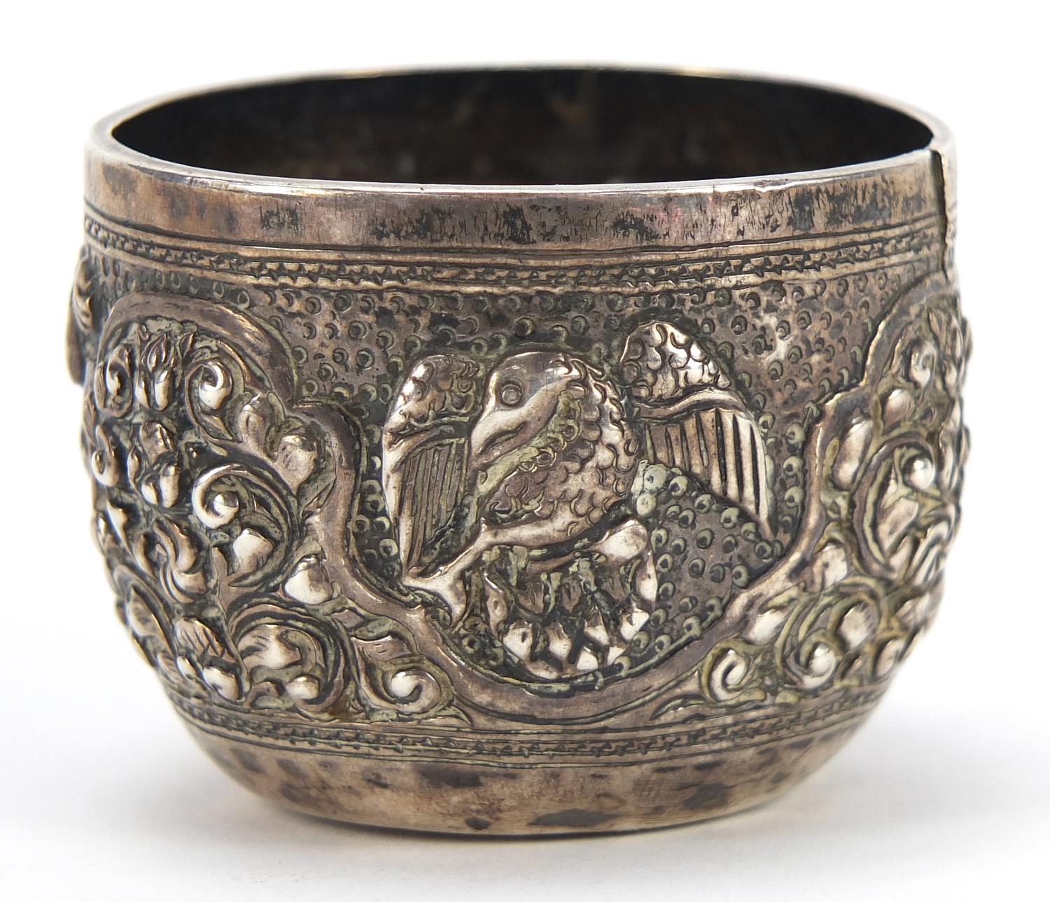 Tibetan silver cup profusely embossed with birds and wild animals amongst foliage, 3.5cm high, 44.4g