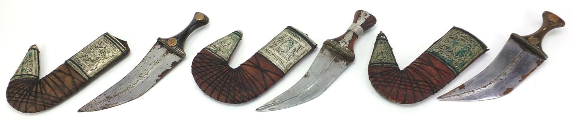 Three Islamic jambiya daggers with horn handles, leather sheaths and white metal mounts, each