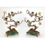 Pair of patinated bronze and porcelain two branch candelabras in the form of birds amongst trees,