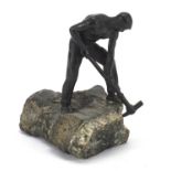 Patinated bronze sculpture of a semi nude man with a pickaxe raised on a naturalistic stone base,