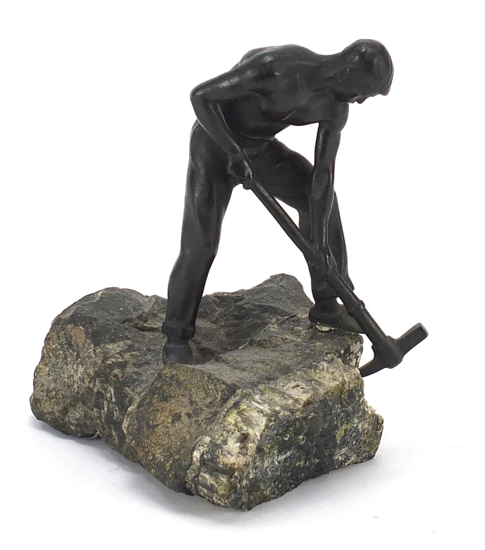 Patinated bronze sculpture of a semi nude man with a pickaxe raised on a naturalistic stone base,