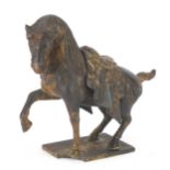 Chinese cast iron horse with one raised foreleg, standing on a metal plinth, 23cm in length