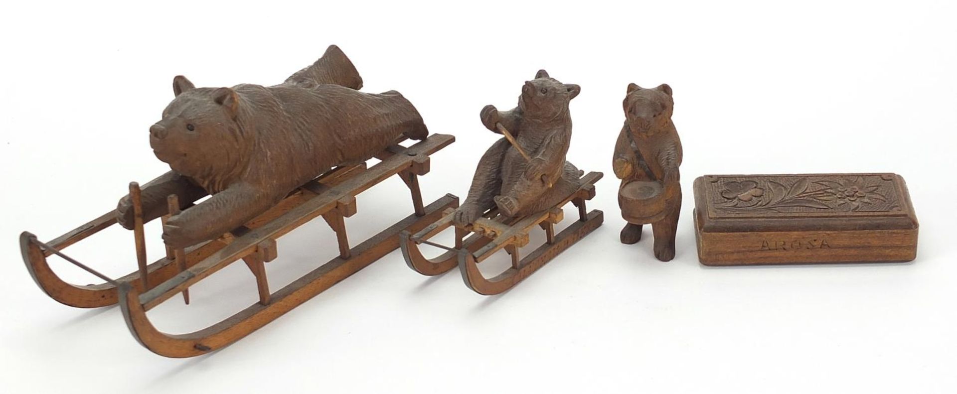 Three carved Black Forest bears and a matchbox including two riding sleds, the largest 15cm in