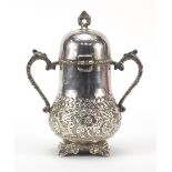 Silver coloured metal vessel with hinged lid and twin handles, 19cm high