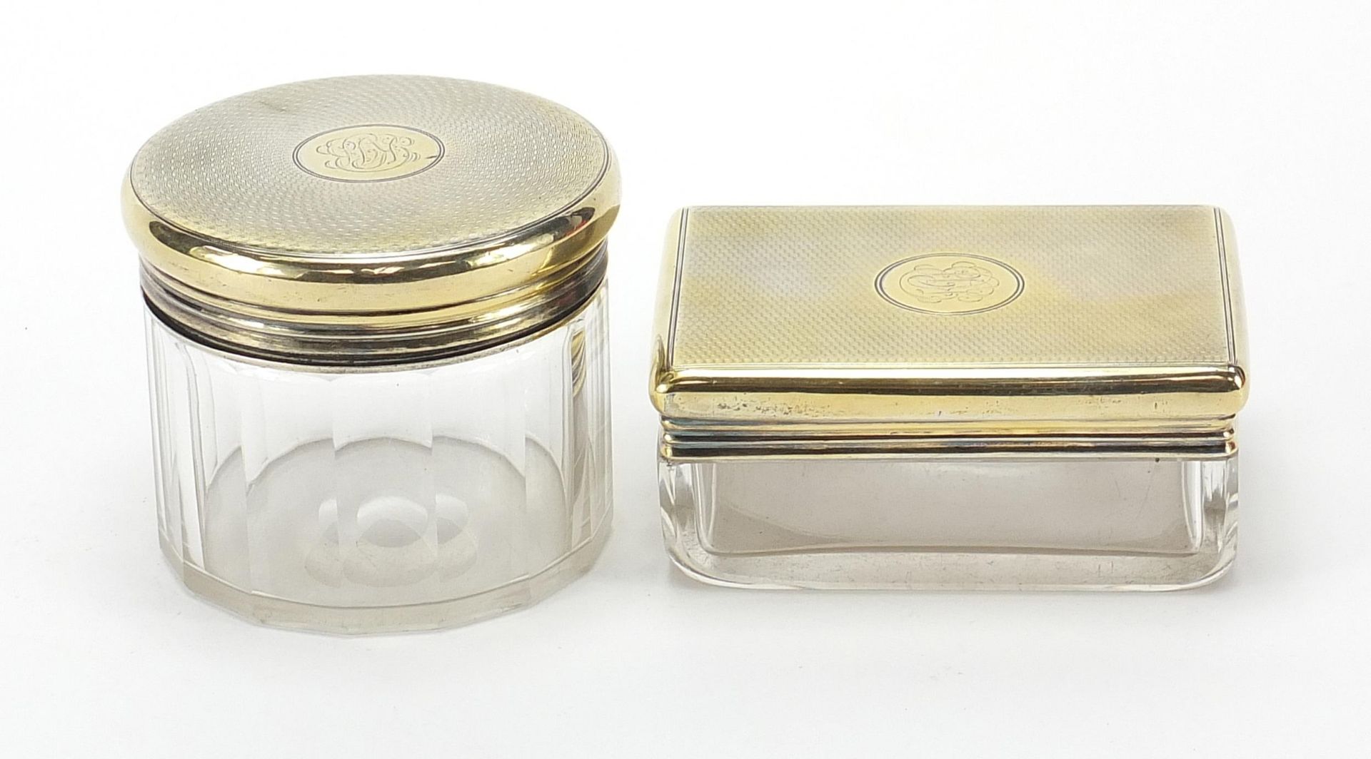 Asprey, two cut glass jars with silver gilt lids and engine turned decoration, the largest 9cm wide