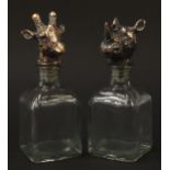 Pair of glass decanters with rhinoceros and giraffe head stoppers, 24cm high