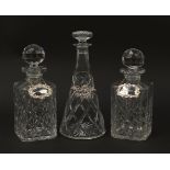 Three cut glass decanters with labels including two silver examples, the largest 29cm high