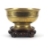 Chinese bronze footed bowl engraved with flowers raised on a carved hardwood stand, 25cm in diameter