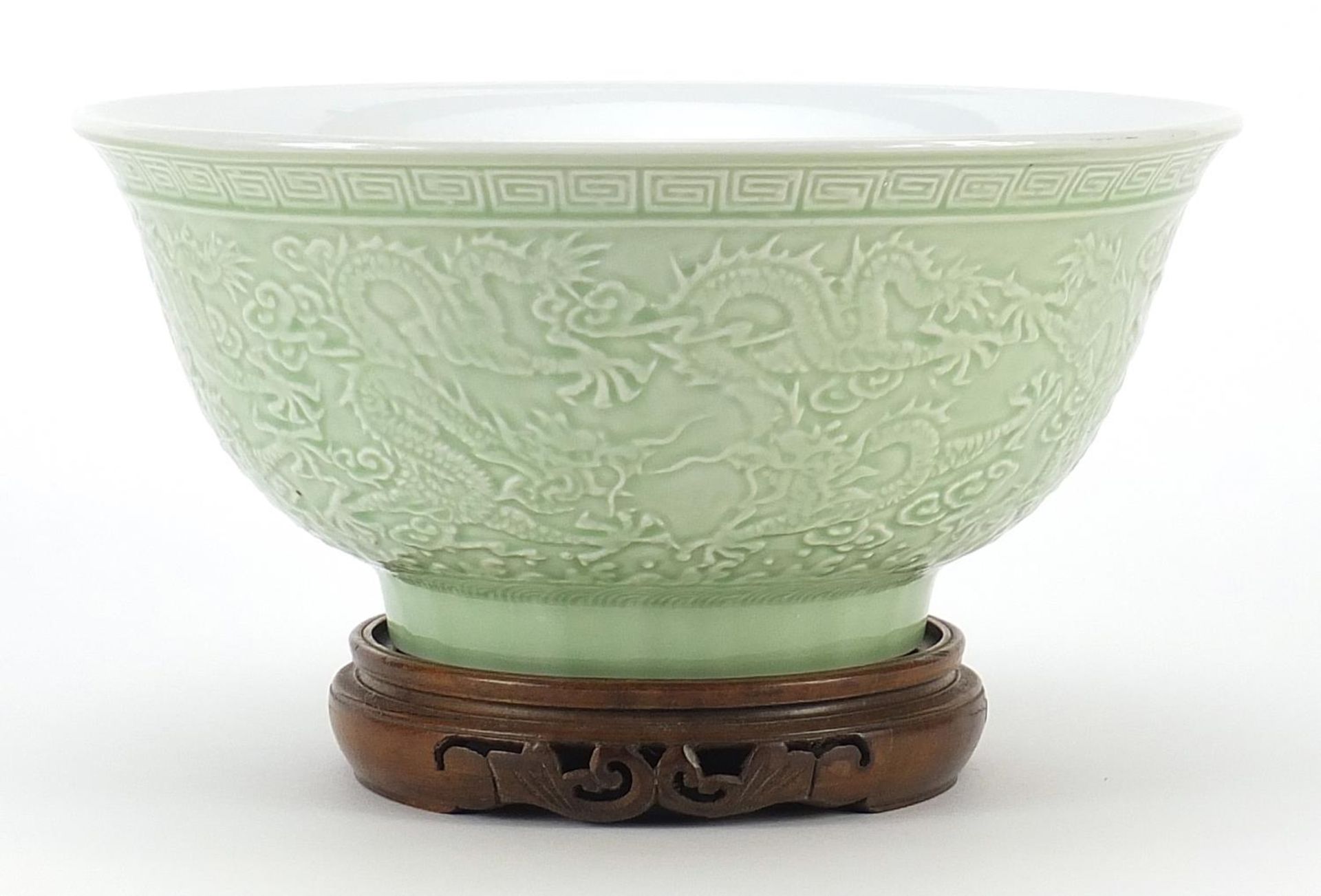 Chinese porcelain bowl raised on hardwood stand having a celadon glaze, decorated in relief with