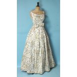 A 1950's ivory floral brocade evening dress, sleeveless, with full pleated skirt and bow waist band,