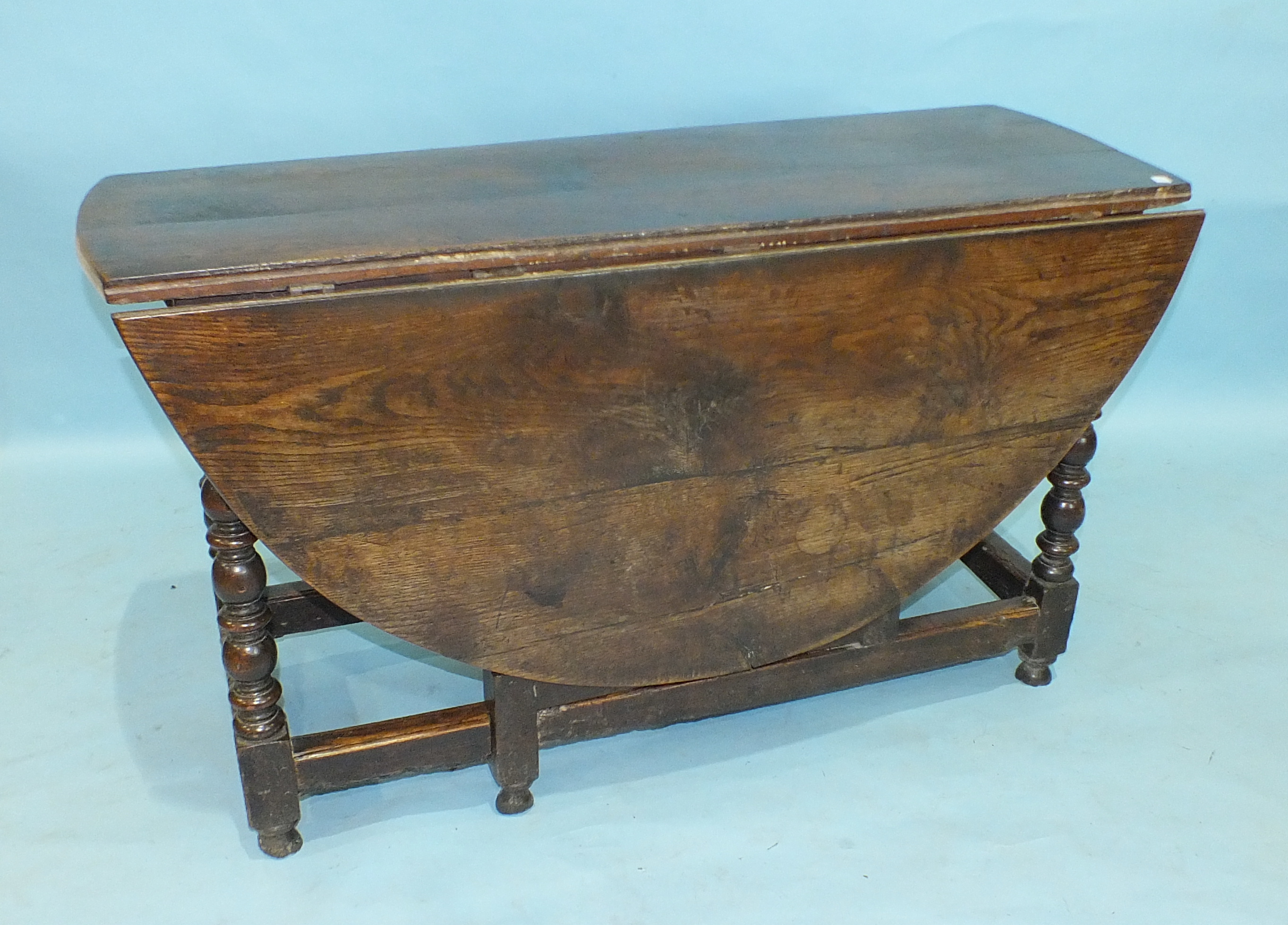 An antique oak drop-leaf dining table, the oval top above an end frieze drawer, raised on bobbin-