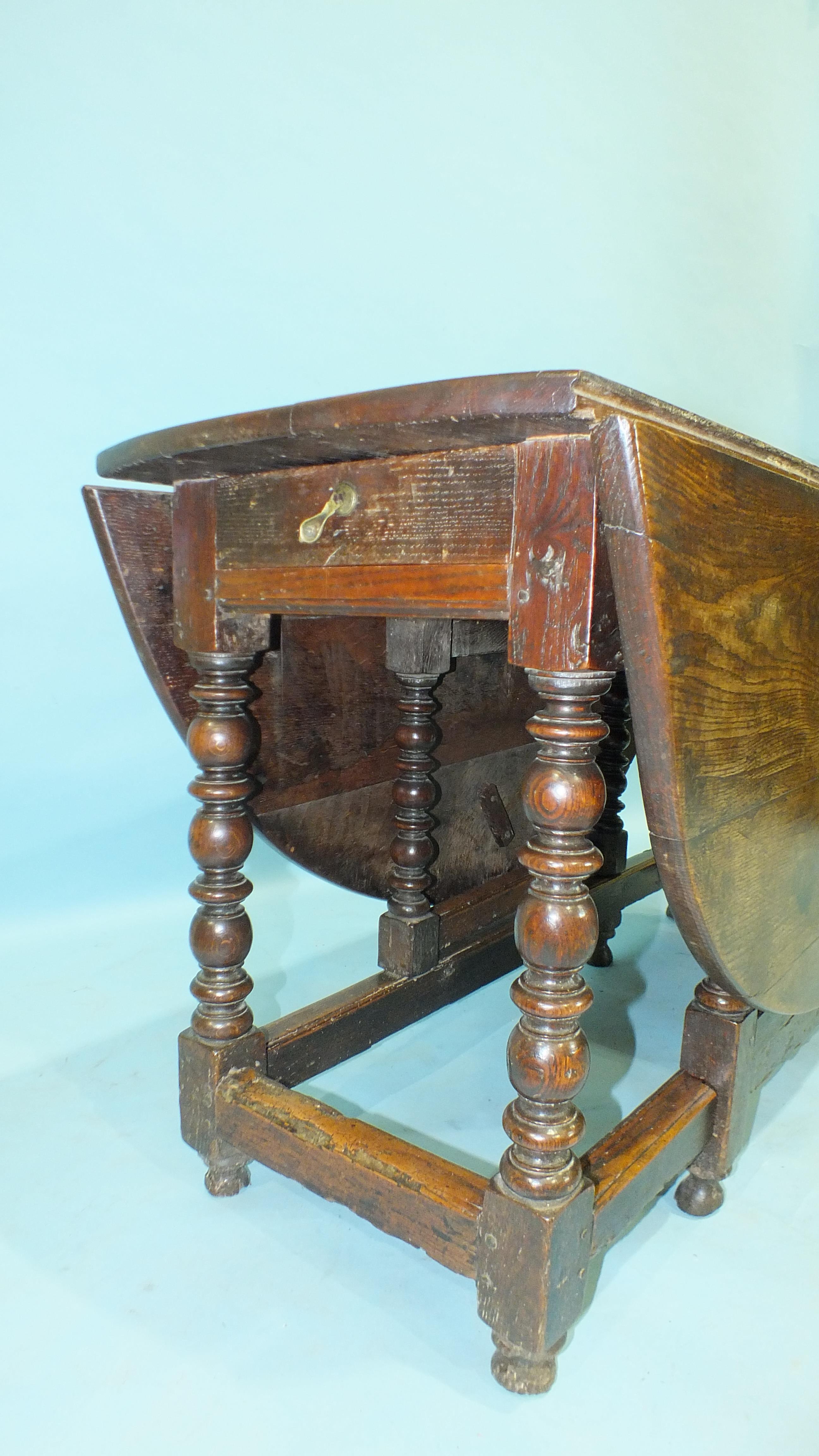 An antique oak drop-leaf dining table, the oval top above an end frieze drawer, raised on bobbin- - Image 3 of 3