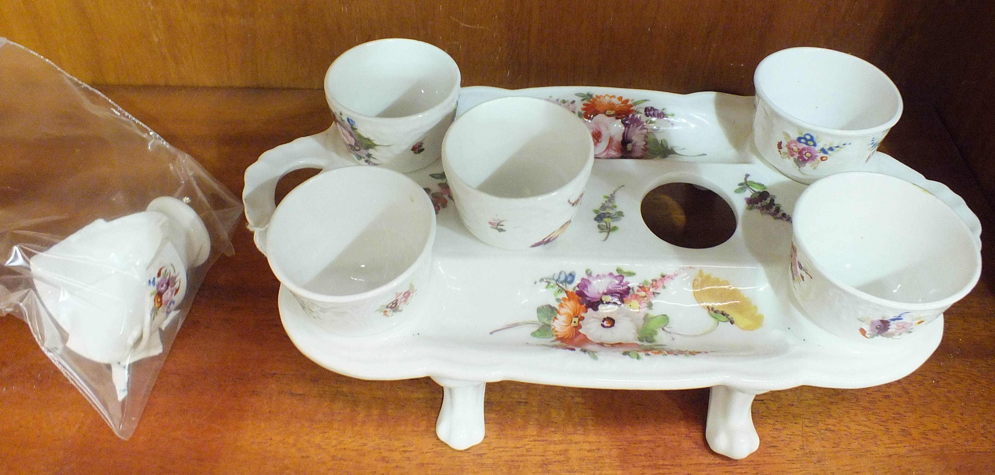 A mid-19th century English porcelain egg cup stand with six matching egg cups (one broken), on paw