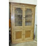A pine corner cupboard, the moulded cornice above a pair of glazed doors and a pair of cupboard