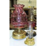 A reproduction oil lamp with cranberry glass reservoir and brass column on ceramic plinth, a