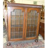 A mid-20th century oak bookcase, the rectangular top above a pair of leaded glass doors on bun feet,