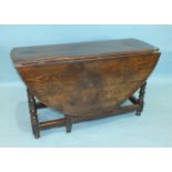 An antique oak drop-leaf dining table, the oval top above an end frieze drawer, on bobbin-turned