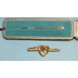 A pearl-topped gold stick pin in fitted case and a lover's knot brooch with central screw