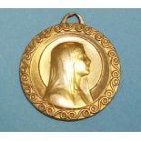 A yellow metal circular pendant with raised head and shoulders of the Virgin Mary within scrolling