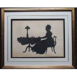 A large silhouette picture of a Victorian lady writing at a tripod table supporting a lamp, inkstand