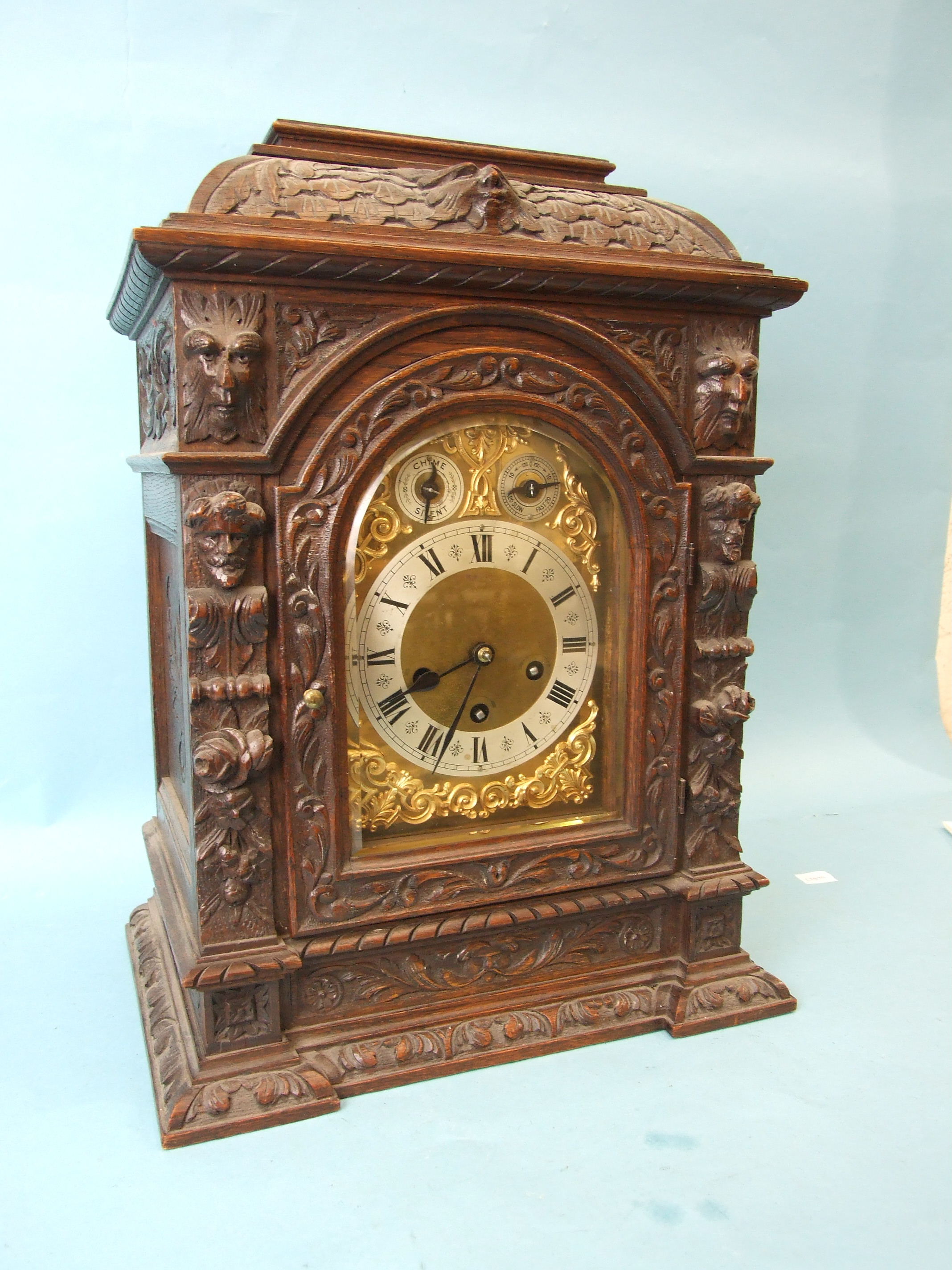 An Edwardian carved oak bracket clock, the arched gilt brass dial with silvered chapter ring, slow/