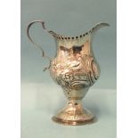 A George III silver cream jug of baluster form, with embossed floral decoration around a vacant
