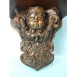 An oak wall bracket incorporating an antique carved cherub's head surrounded by foliage and drapery,
