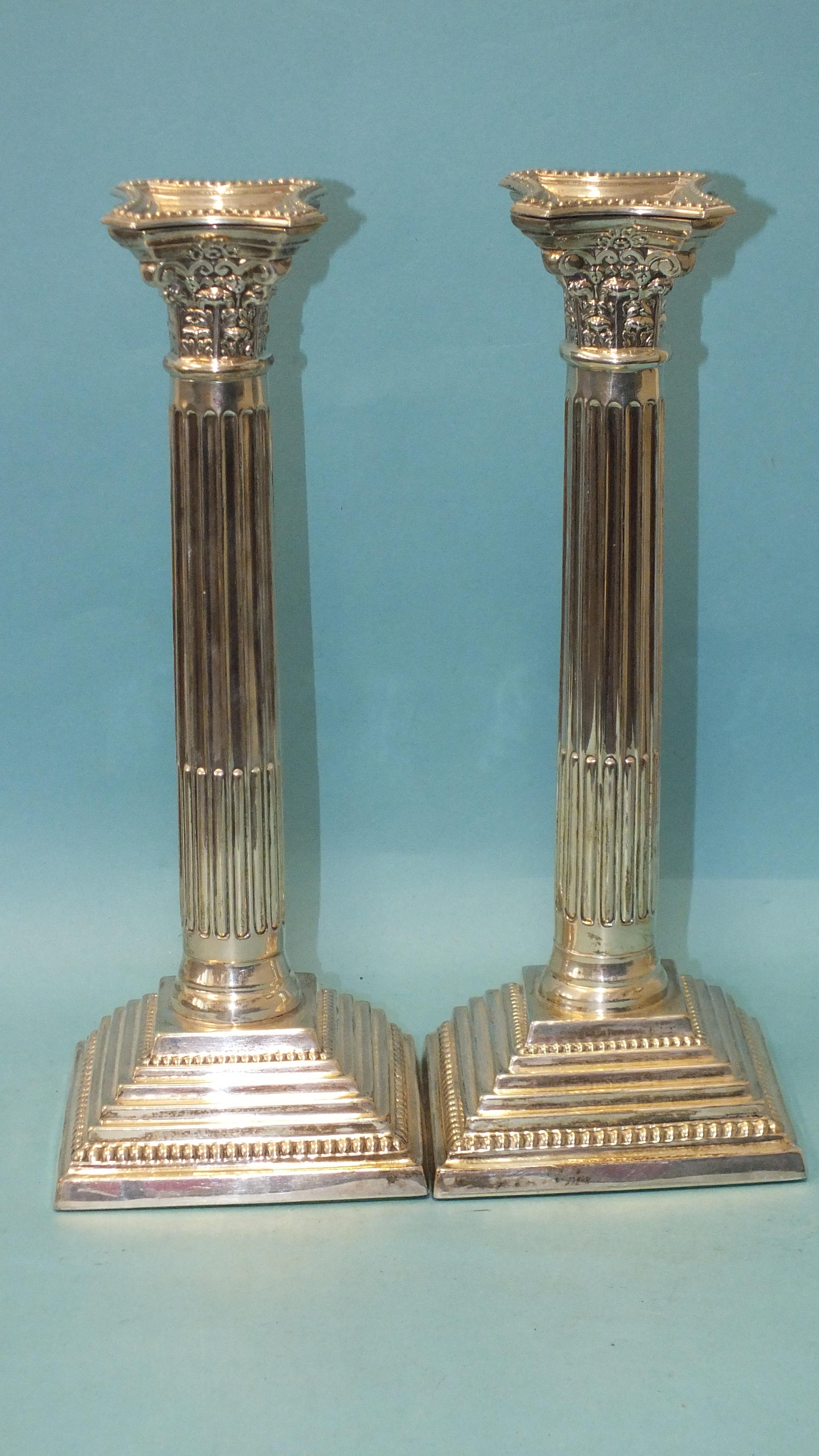 A pair of loaded silver Corinthian column candlesticks on stepped and beaded square bases, with drip