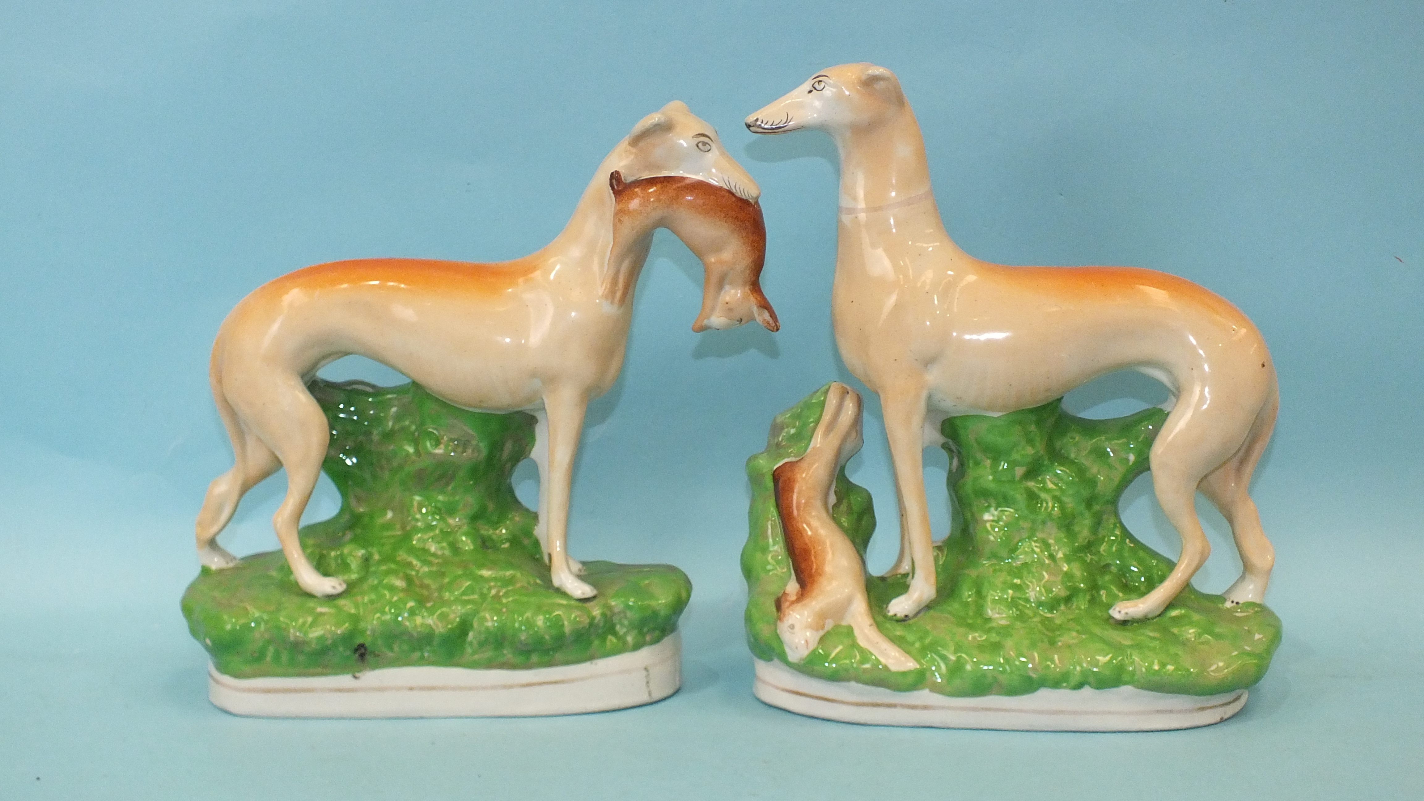 A pair of 19th century Staffordshire pottery figures of greyhounds, each standing, one with a hare