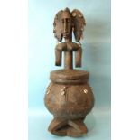 An African carved wood pot and cover, the triple-head finialled lid and bellied pot hung with cowrie