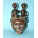 A carved hardwood female mask surmounted by male and female figures of children arm-in-arm, 25cm