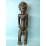 A large African carved wood male figure, standing with hands on his stomach and with carved hair and