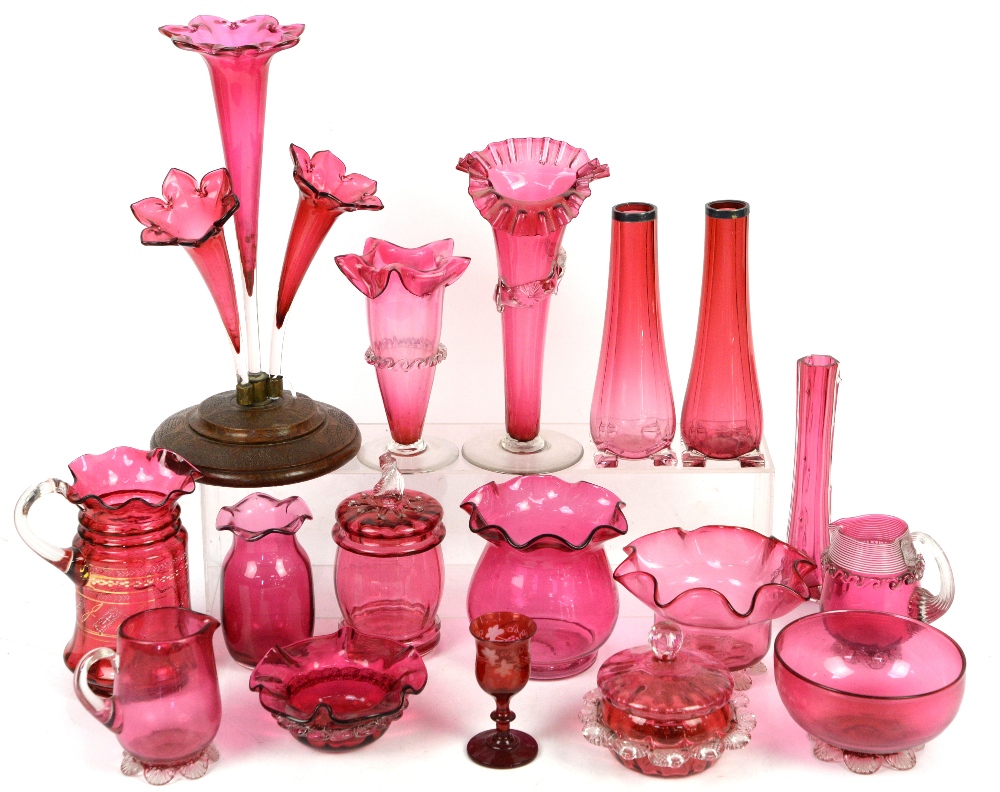 Collection of cranberry glass items including jugs, vases and pot with cover