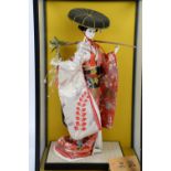 Japanese Geisha doll, dressed in red and white kimono and jewelled black hat, in glass case h53cm,