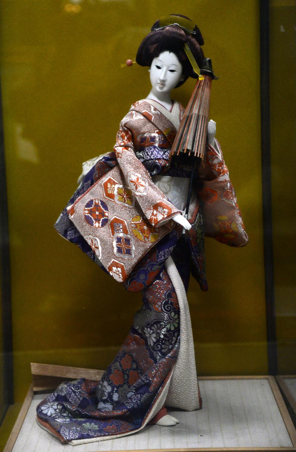 Large Japanese Geisha doll, wearing coral and blue kimono and holding a parasol, in glass case h63.