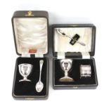 Two piece silver egg cup and spoon, cased and a similar three piece plated cased christening set