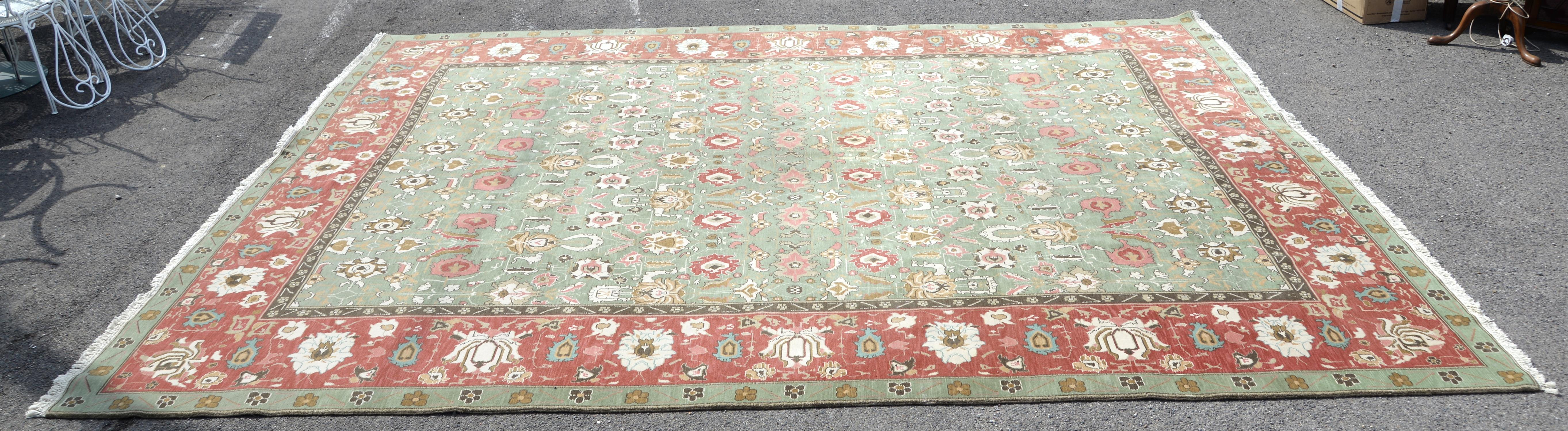 Agra Carpet with repeating floral motifs on a green ground, within a red ground border with floral